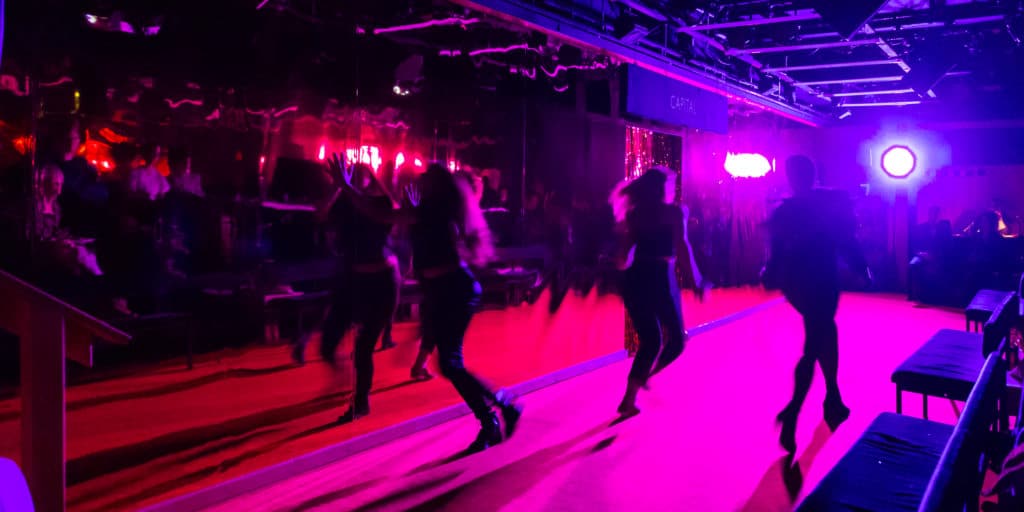 Production photo of Mephisto [A Rhapsody] showing people stood up and running around the space dimly lit against bright colourful LEDs