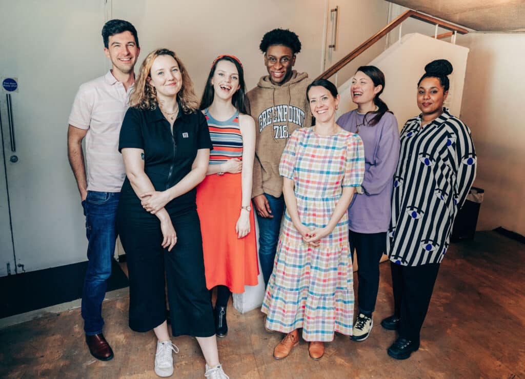 Ed Borgnis, Alice Linnane, Isabelle Culkin, Wofai JE, Katherine de Halpert, Stef O'Driscoll, and Faiza Abdulkadir stand smiling as a group in the Gate Theatre foyer